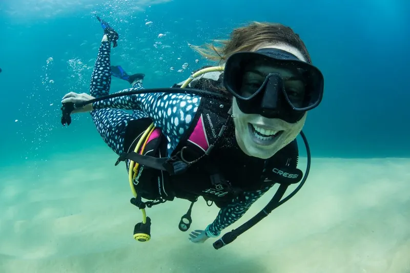 Plongeuse souriante en combinaison, nageant dans une eau turquoise claire