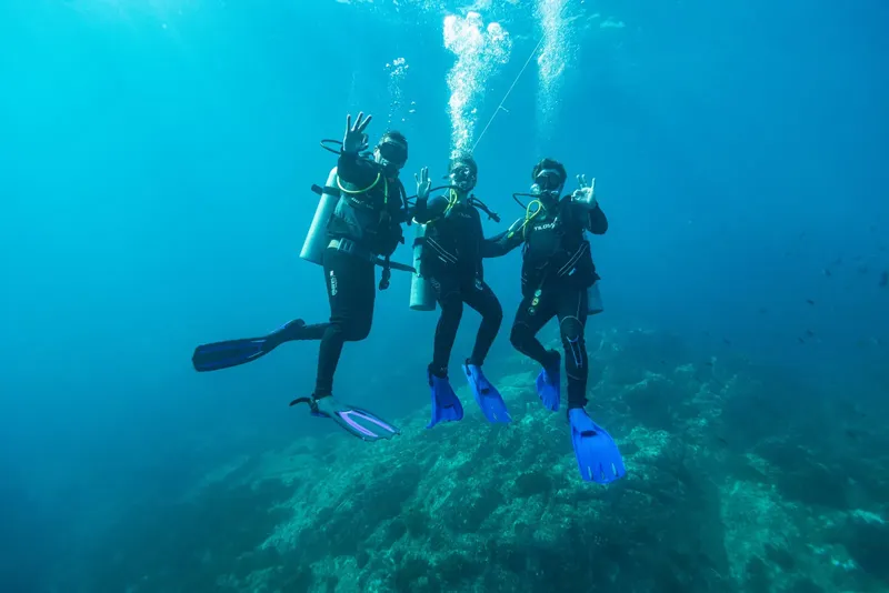 Trois plongeurs souriants font des signes de la main sous l'eau