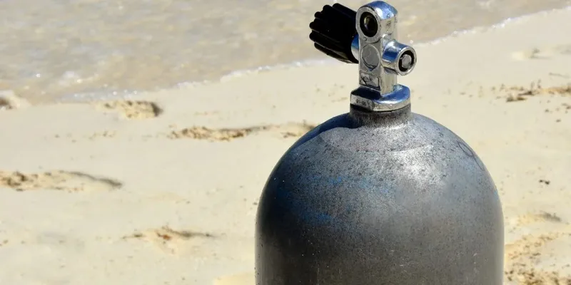 Bouteille de plongée noire sur sable avec robinet chromé brillant