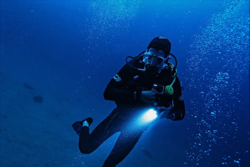 Plongeur en combinaison noire, lampe torche, dans l'eau bleue