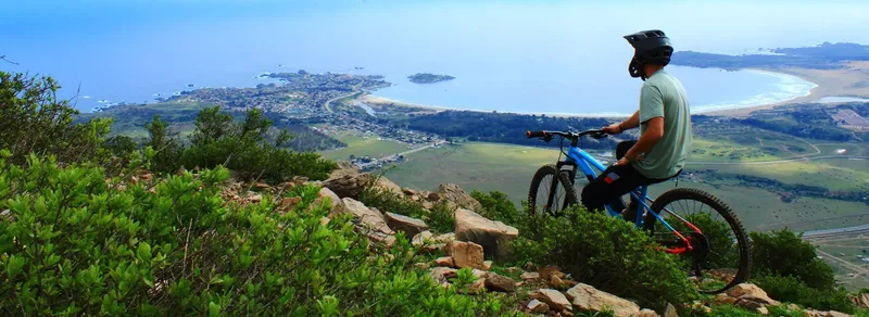 Homme à vélo de montagne surplombe une ville côtière ensoleillée