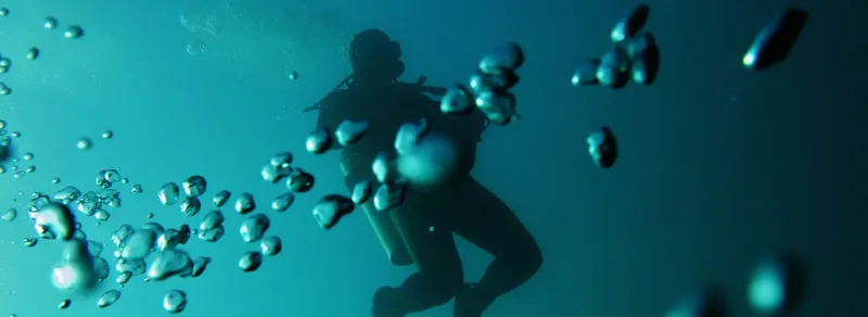 Plongeur en silhouette, entouré de bulles dans l'eau bleue