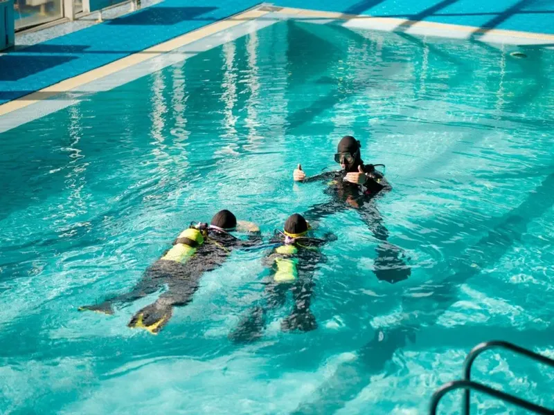 Trois plongeurs en formation dans une piscine, un donne le signe OK