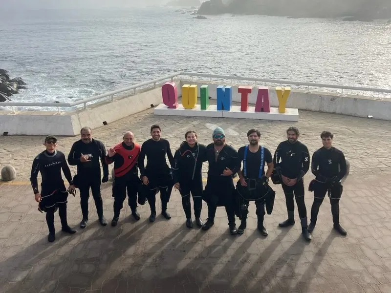 Groupe de plongeurs en combinaison devant une inscription colorée au bord de mer