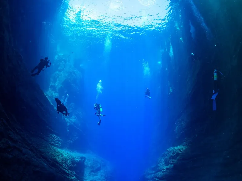Plongeurs explorant une grotte sous-marine, lumière filtrant en surface