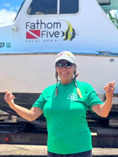 Femme souriante devant un bateau de plongée avec le logo du centre