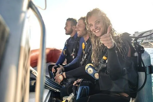 Trois plongeurs souriants à bord d'un bateau, équipés et prêts