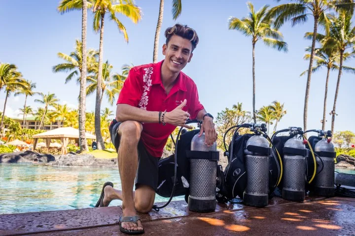 Un homme souriant à genoux près de bouteilles de plongée
