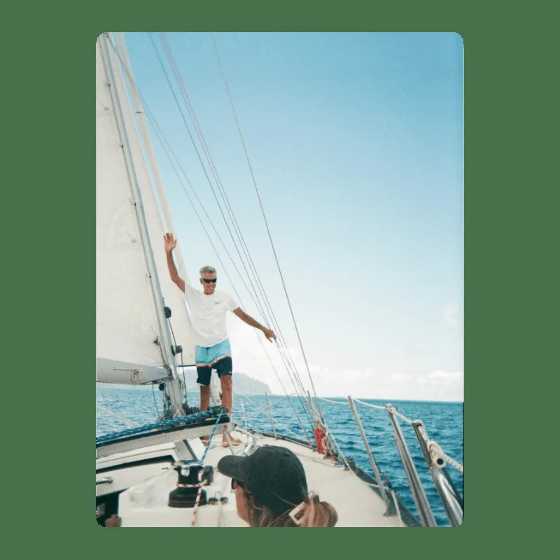 Homme sur un voilier, bras levé, mer bleue et ciel clair