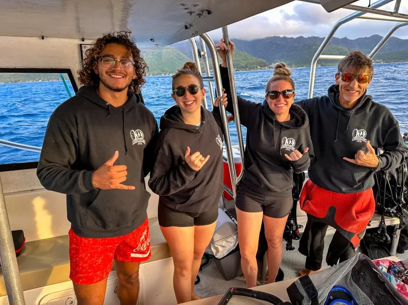Quatre personnes souriantes sur un bateau en mer, faisant des signes