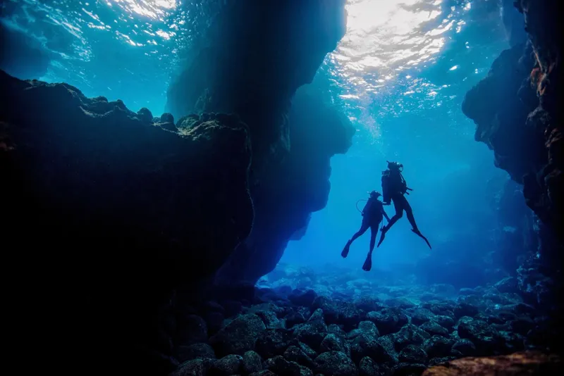 Deux plongeurs explorent une grotte sous-marine éclairée par le soleil