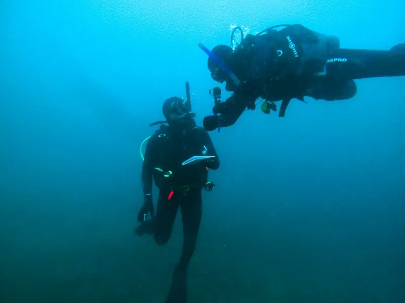 Deux plongeurs en combinaison communiquent sous l'eau dans une ambiance bleutée