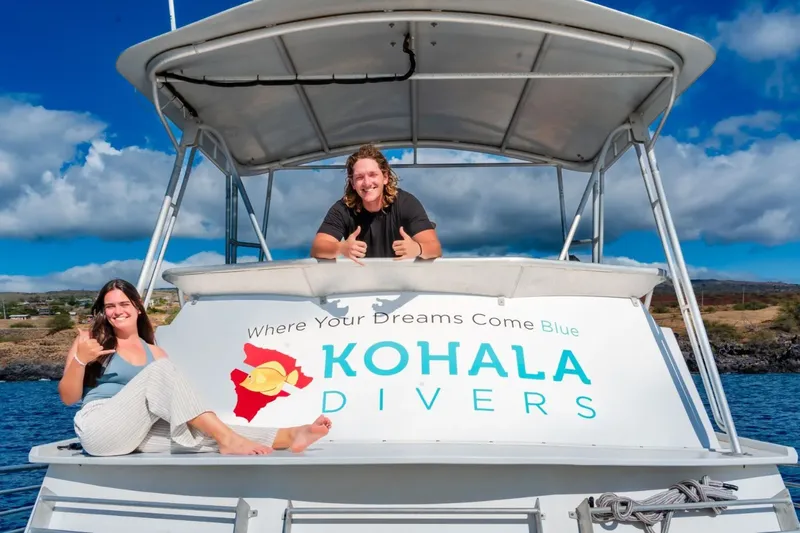 Deux personnes souriantes sur un bateau de plongée bleu et blanc