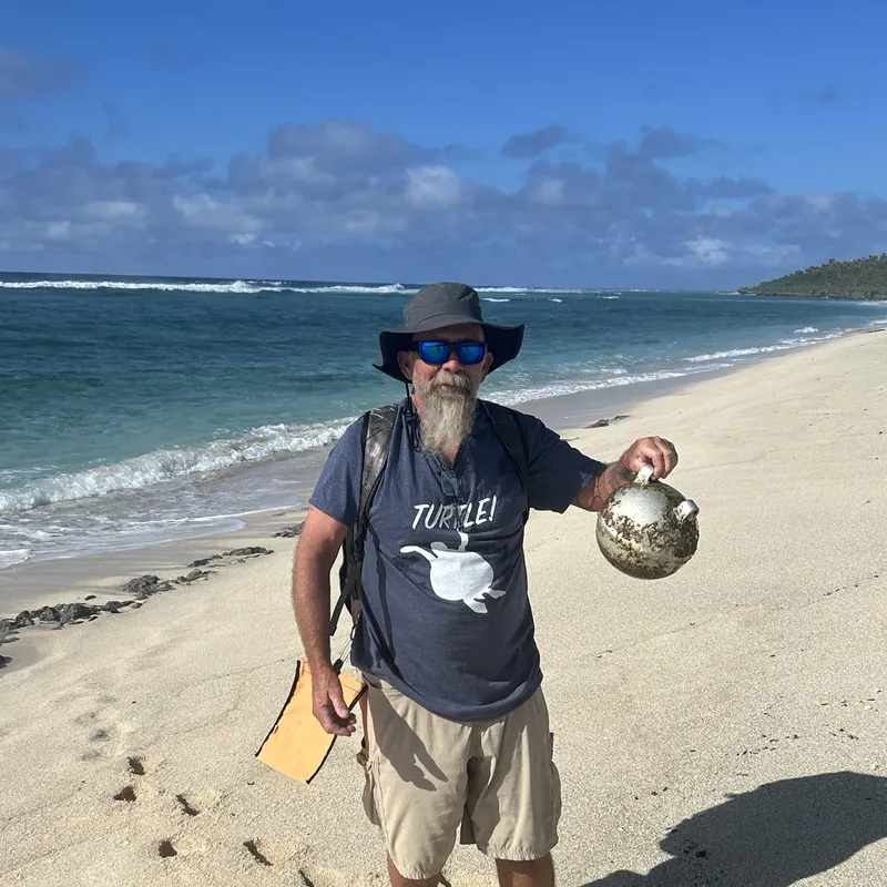 Homme sur une plage tient une coquille marine, portant un t-shirt