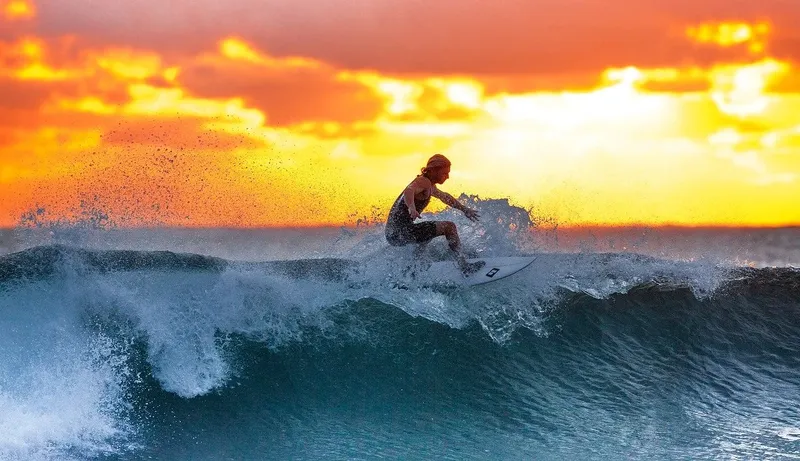 Surfeur sur une vague au coucher du soleil, eau turquoise et ciel flamboyant