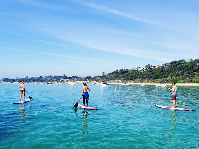 Trois personnes pratiquent le stand-up paddle dans une eau turquoise