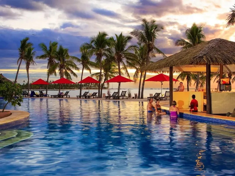Personnes au bar d'une piscine avec palmiers et coucher de soleil