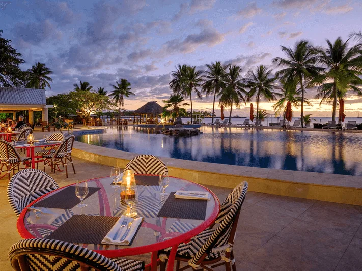 Tables dressées au bord d'une piscine avec coucher de soleil en arrière-plan