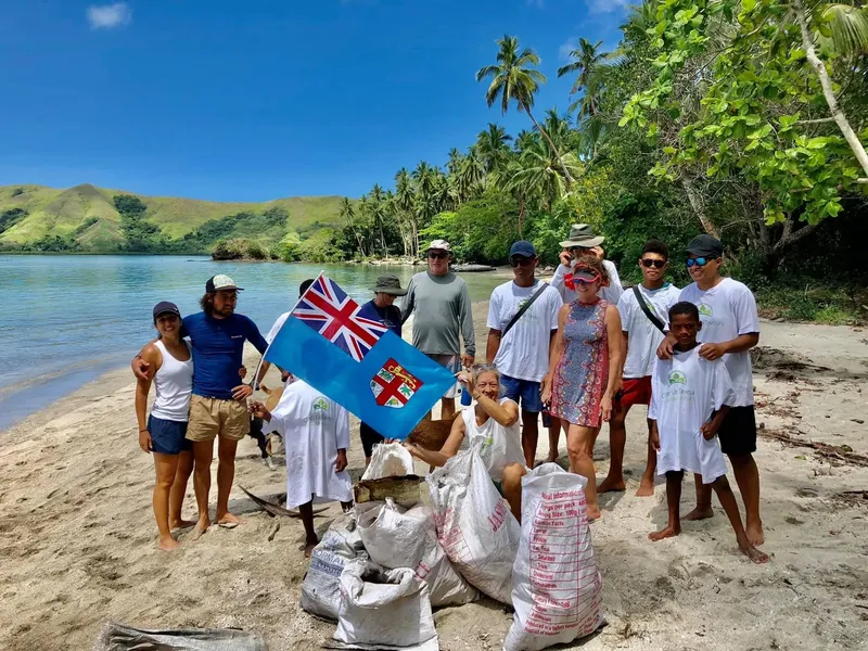 Groupe de personnes souriantes sur une plage avec des drapeaux et sacs