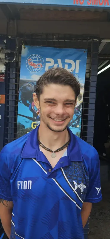 Jeune homme souriant portant un polo bleu devant une bannière PADI