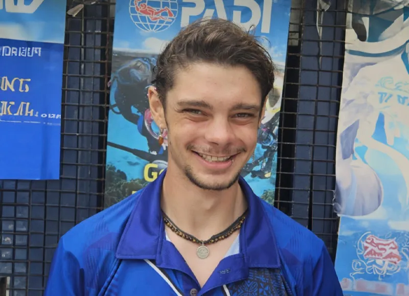 Jeune homme souriant devant une affiche de plongée sous-marine PADI