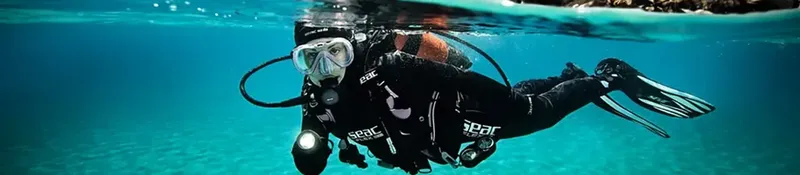 Plongeur en combinaison noire nageant sous la surface de l'eau bleue