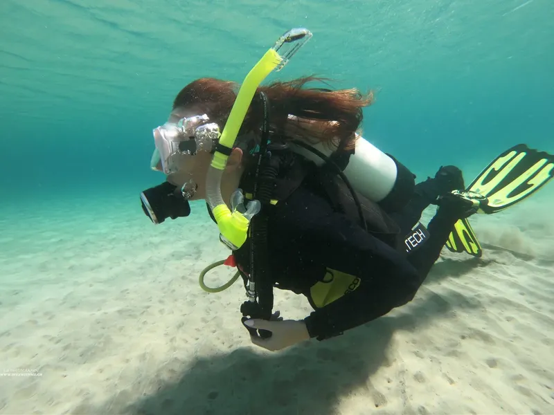 Plongeuse manipule son appareil photo sous l'eau, fond sableux clair