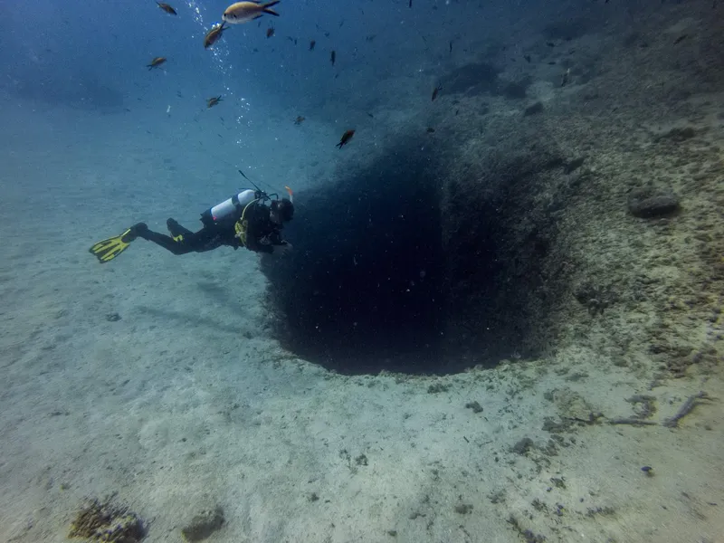 Plongeur explorant une grotte sous-marine avec des poissons alentour