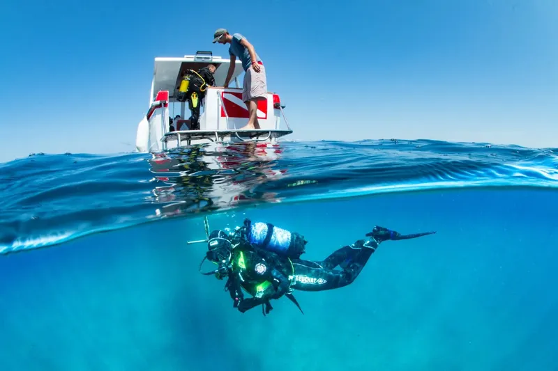 Plongeur en exploration sous un bateau, eau claire et ciel bleu