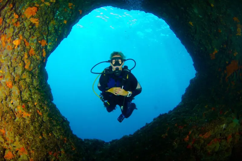Plongeur explorant une ouverture rocheuse sous-marine en combinaison complète