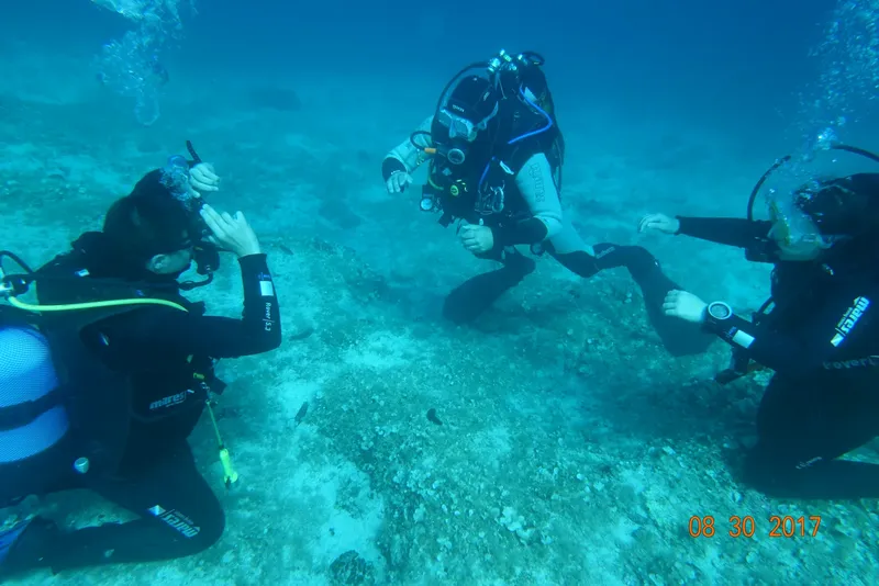 Trois plongeurs en combinaison noire évoluent sous l'eau sur fond sableux