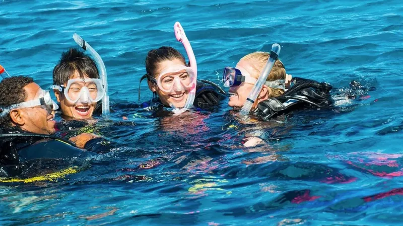 Quatre plongeurs souriants, masques et tubas, dans une eau bleue claire