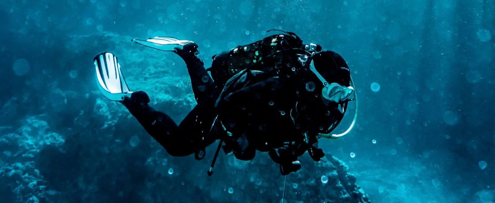Plongeur en combinaison noire nageant dans une eau bleu profond