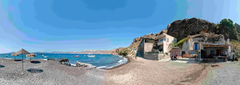 Plage de galets, bâtiments blancs, bateaux en mer et parasols ouverts