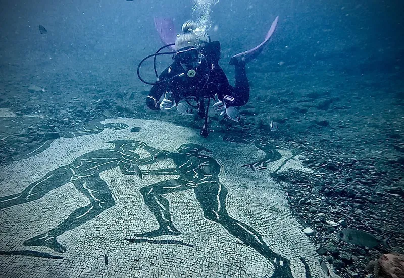Plongeuse explorant une mosaïque antique sous-marine avec des pouces levés