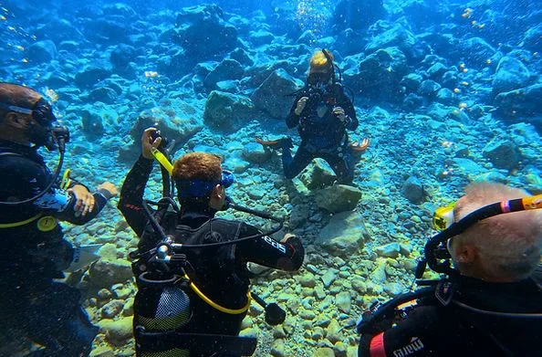 Plongeurs interagissent sous l'eau au milieu d'un paysage rocheux et sablonneux