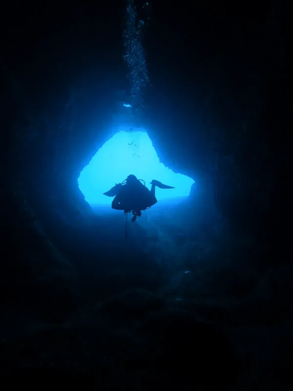 Plongeur silhouette sombre explorant une grotte sous-marine éclairée par le soleil