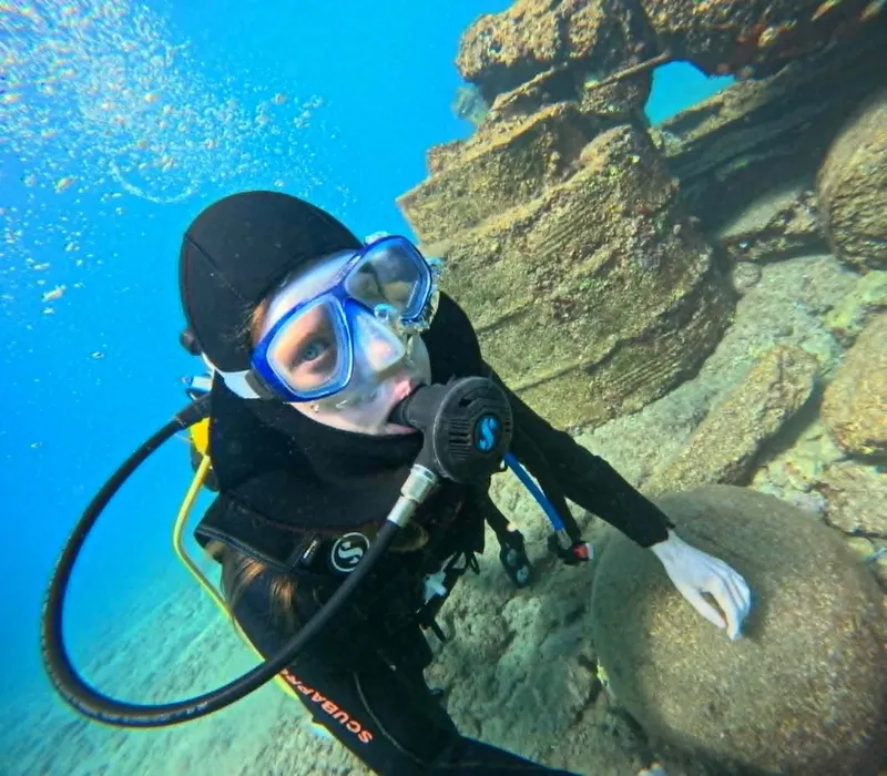 Plongeuse souriante avec masque et détendeur en milieu aquatique rocheux
