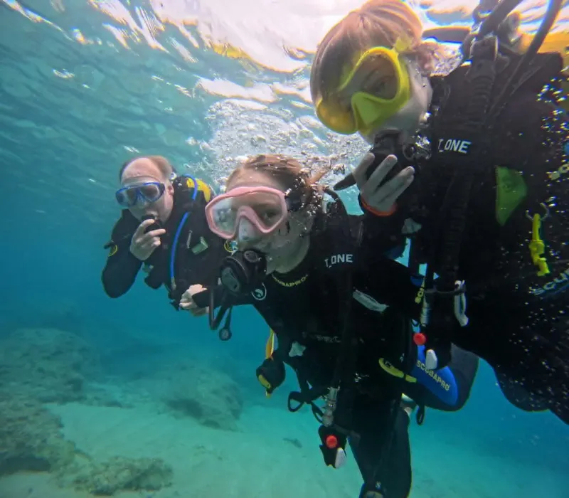 Trois plongeurs souriants avec leur équipement complet sous l'eau