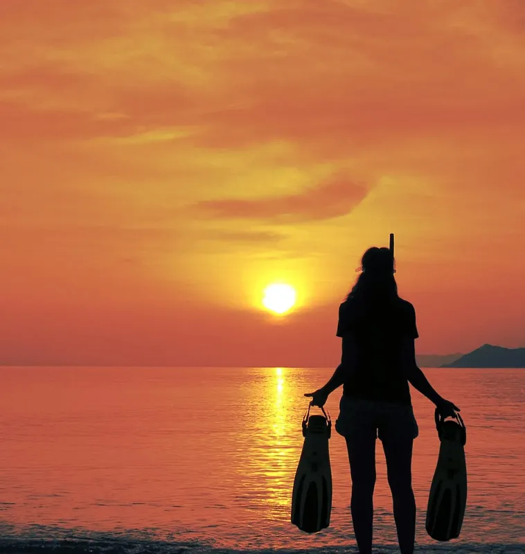 Silhouette plongeuse au coucher du soleil avec palmes et masque