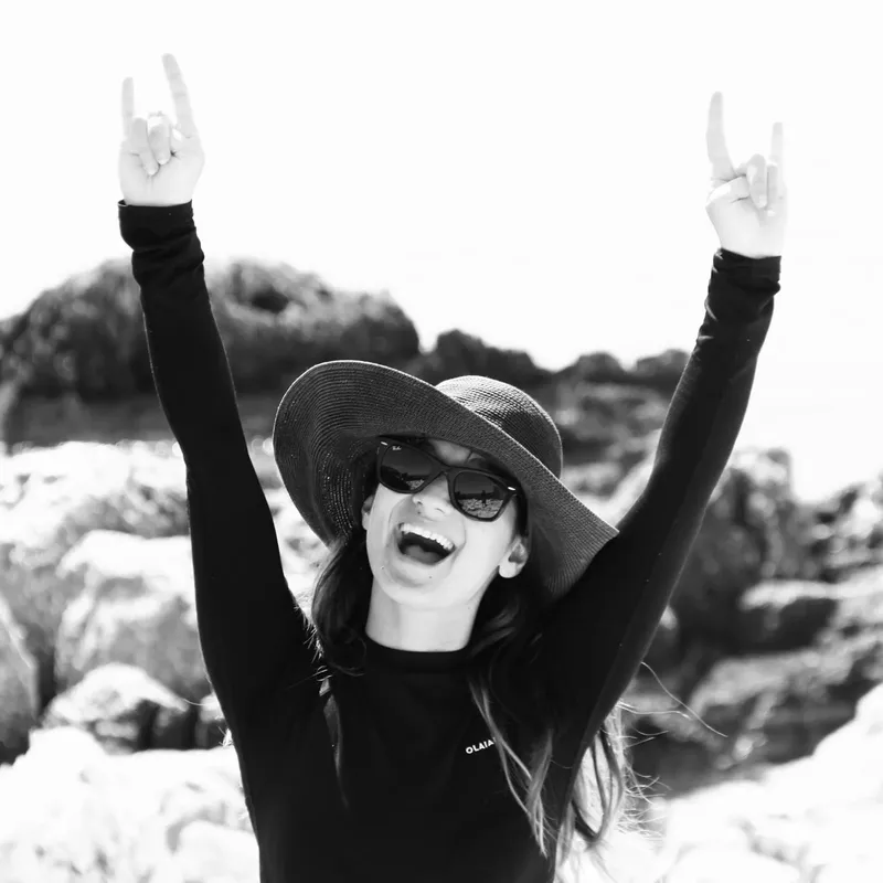 Femme souriante, chapeau et lunettes de soleil, bras levés en signe de joie
