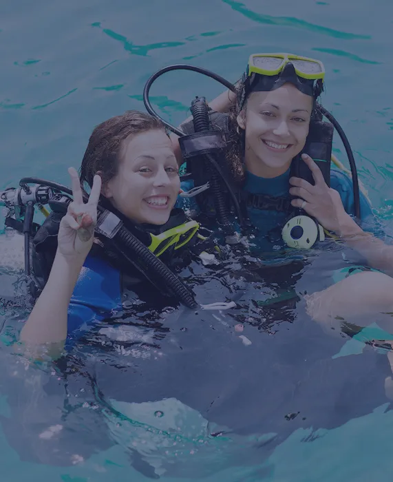 Deux plongeuses souriantes avec leur équipement dans l'eau turquoise