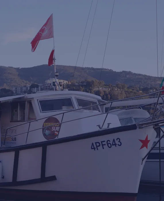 Bateau de plongée blanc amarré au port avec drapeau rouge et montagnes