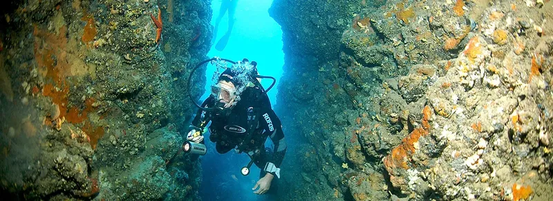 Plongeur explorant une grotte sous-marine rocheuse avec équipement complet