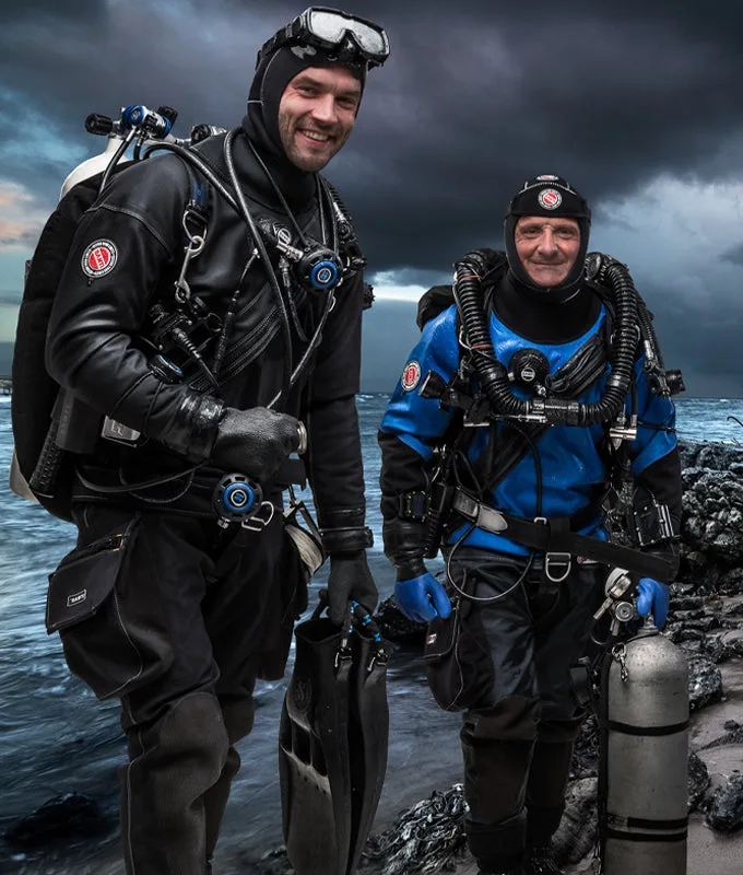 Deux plongeurs souriants équipés sur un rivage rocheux sombre