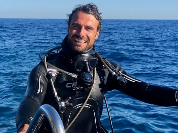 Plongeur souriant en combinaison, masque et détendeur sur fond marin