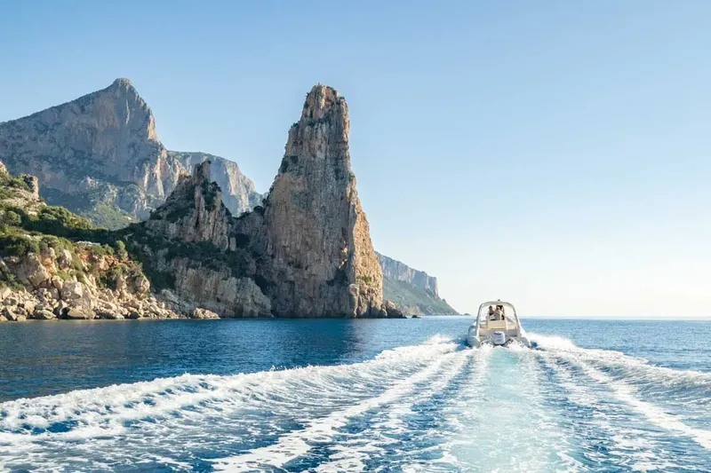 Bateau rapide naviguant vers une côte rocheuse et montagneuse ensoleillée