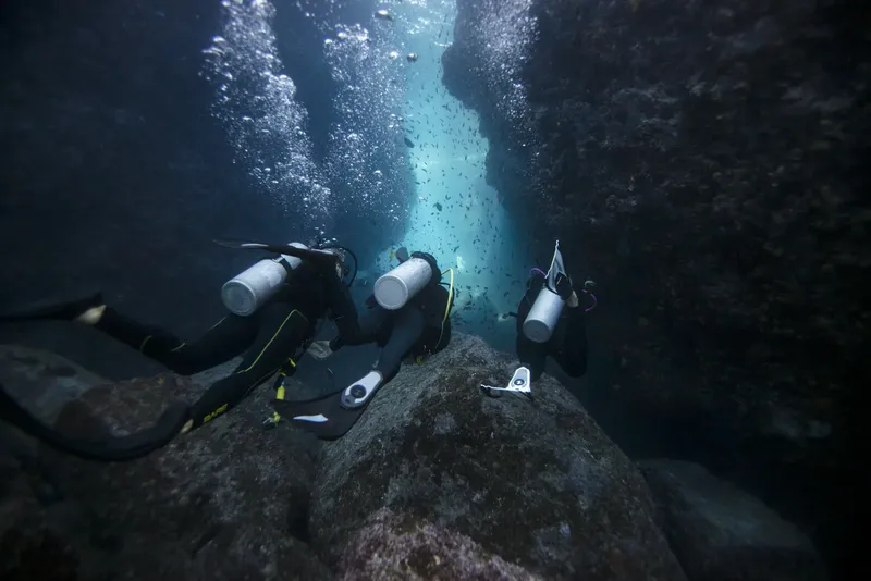 Trois plongeurs explorent une grotte sous-marine avec une lumière bleutée