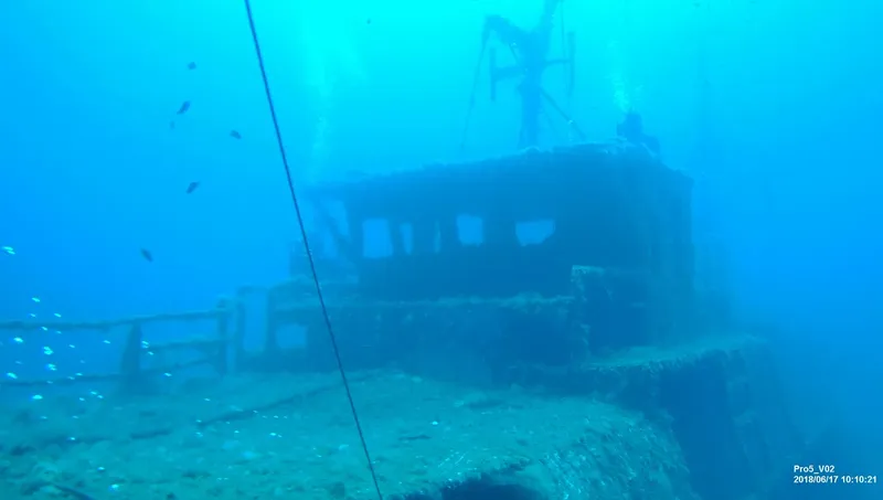 Épave de bateau immergée dans une eau bleue, quelques poissons présents