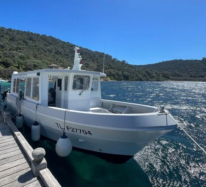 Bateau blanc amarré à un ponton en bois, mer et collines en arrière-plan